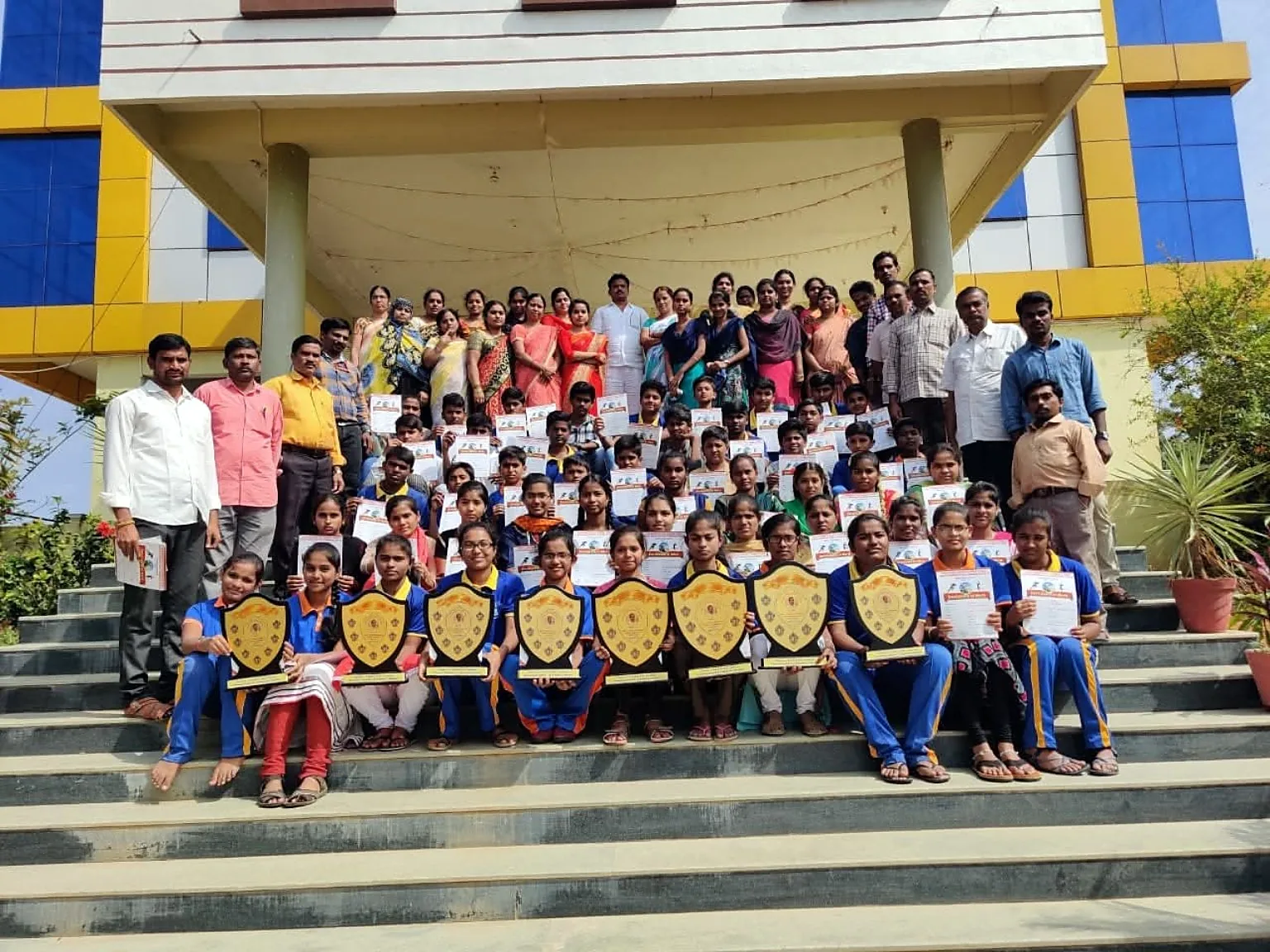 Blue Moon students with shields and certificates on campus steps